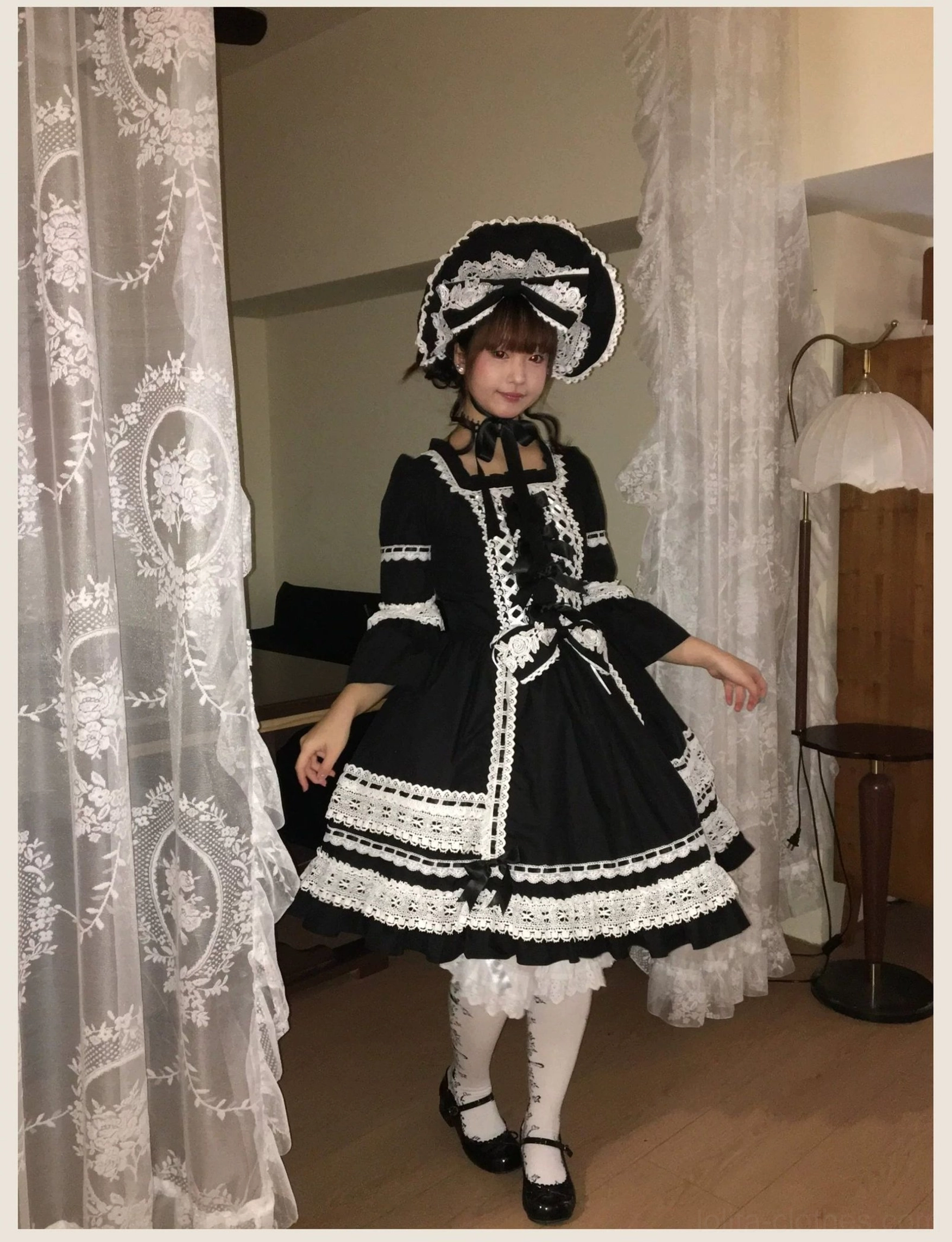 Three-quarter back view of black old school lolita dress with matching bonnet, showing lace-up back closure, layered ruffled underskirt, and Victorian styling