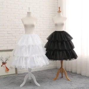 Black adjustable tiered petticoat and white tiered petticoat comparison front eye-level view showing fluffy ruffled tulle silhouette and structural design against brick wall studio backdrop