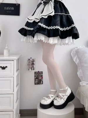 Black and white gothic lolita platform shoes with round toe and cross ankle straps, styled with black-white maid lolita skirt and pink sheer stockings, front lower body view