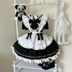 Black and white maid lolita OP dress with bunny ear collar and pom-pom trim displayed on clothing rack, showing front flat view with tiered ruffled skirt and detachable apron