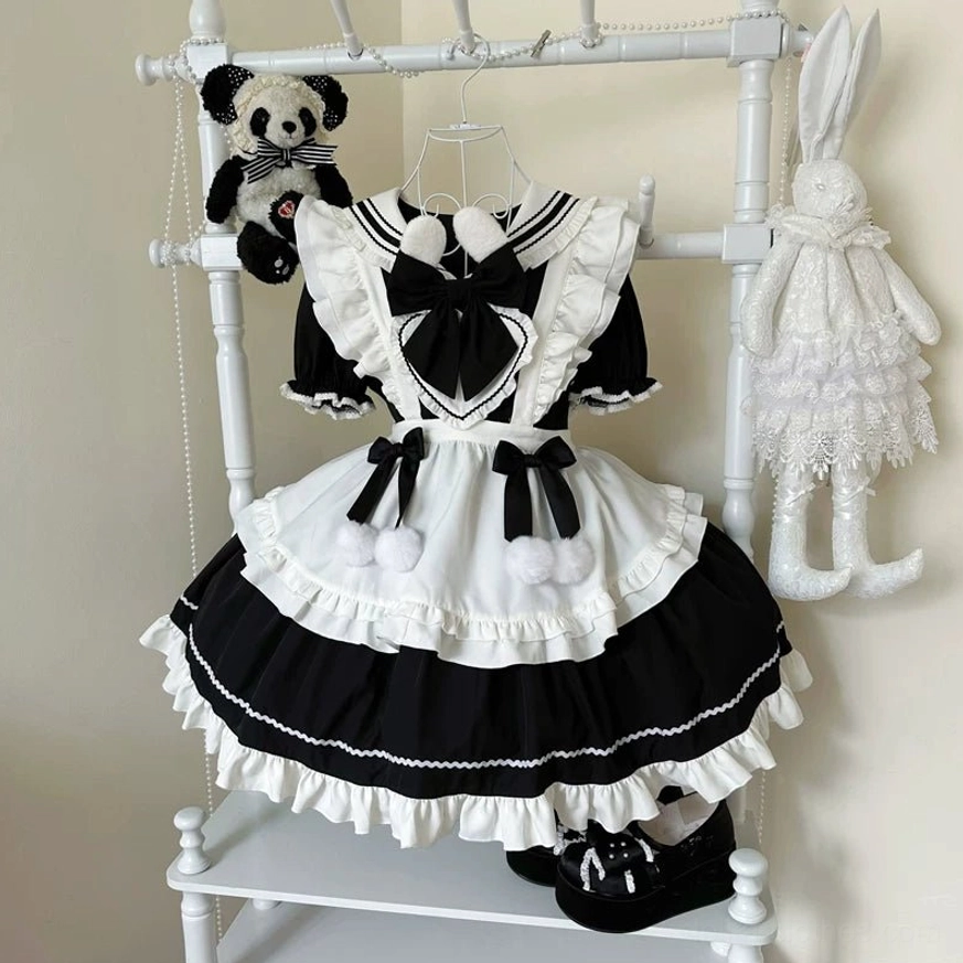 Black and white maid lolita OP dress with bunny ear collar and pom-pom trim displayed on clothing rack, showing front flat view with tiered ruffled skirt and detachable apron
