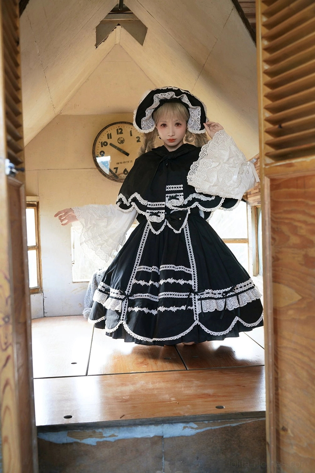 Black and white hooded lolita dress with rabbit ear cape full body indoor shot model vintage attic room wall clock ruffled lace trim bow-decorated hood flared sleeves
