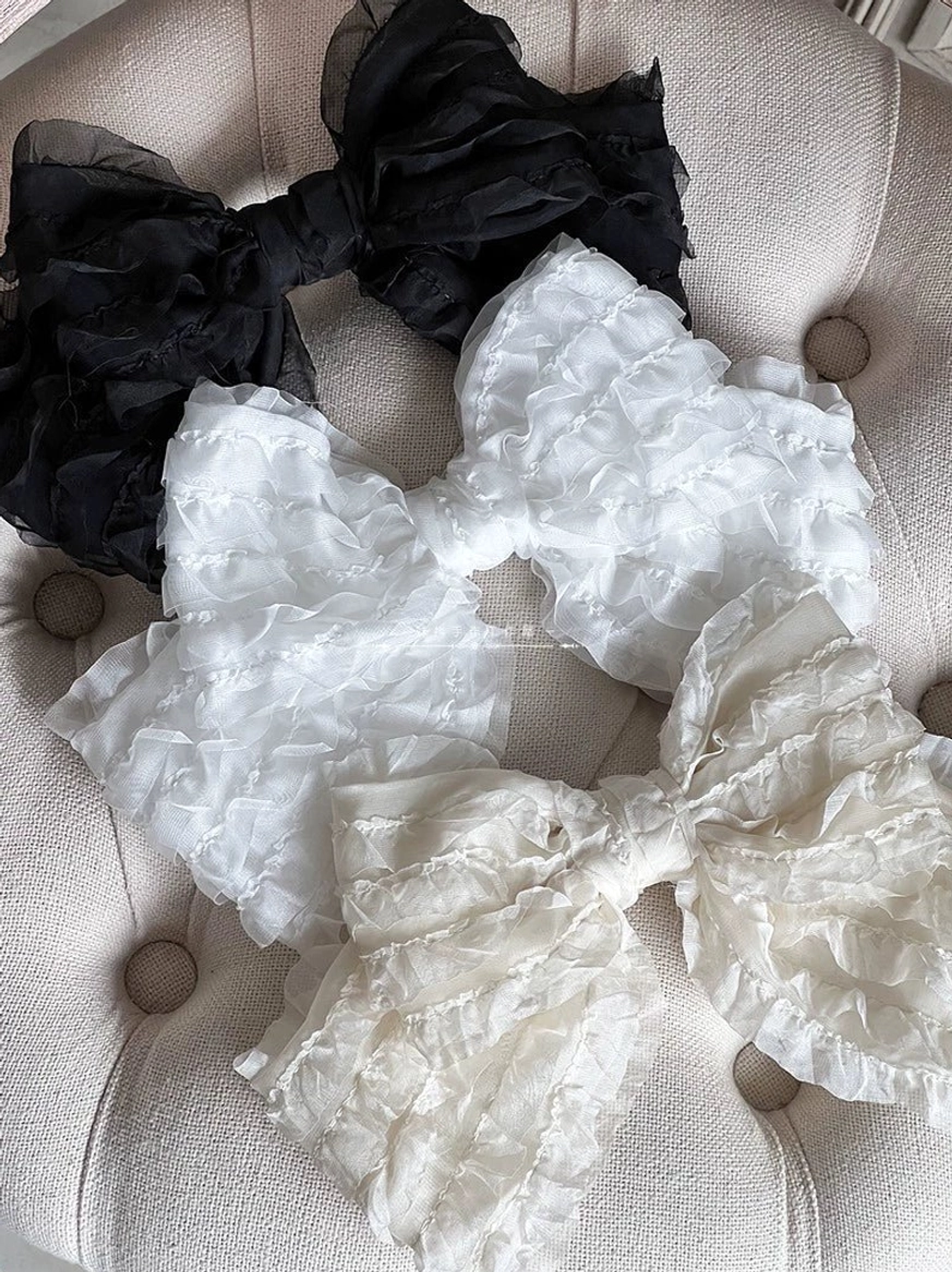 Black and white oversized ruffled organza lolita bow hair clips collection flat lay on tufted beige upholstery