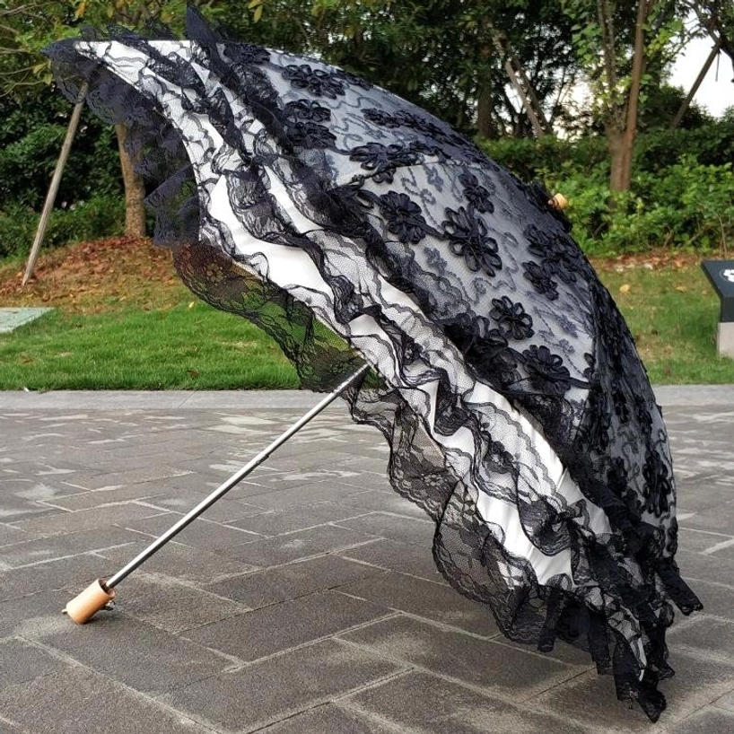 Black and white two-tone lace Lolita sun parasol with sheer black floral outer layer, white inner lining, and ruffled lace edge outdoors with greenery
