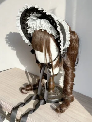 Elegant black and white velvet Lolita bonnet with ruffled lace trim worn on mannequin with brown curly twin ponytail wig, three-quarter front view showing structured brim and decorative ribbon details