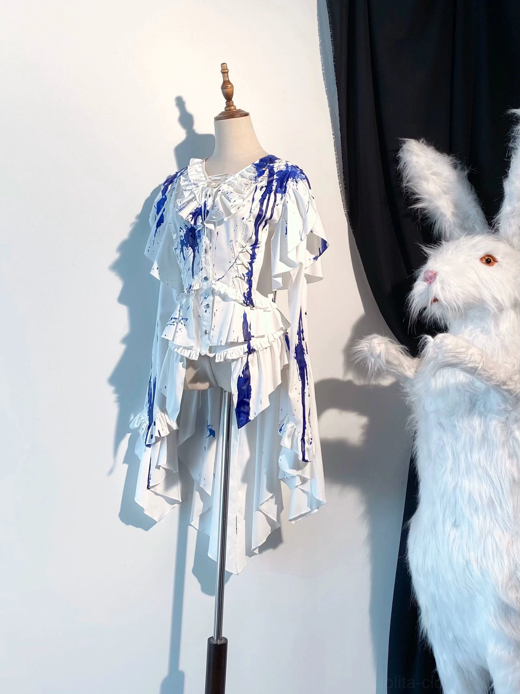 Blue blood-stain Ouji lolita trailing blouse with ocean-inspired splash prints on white satin base, featuring asymmetrical ruffled hem and decorative sleeve panels on mannequin display