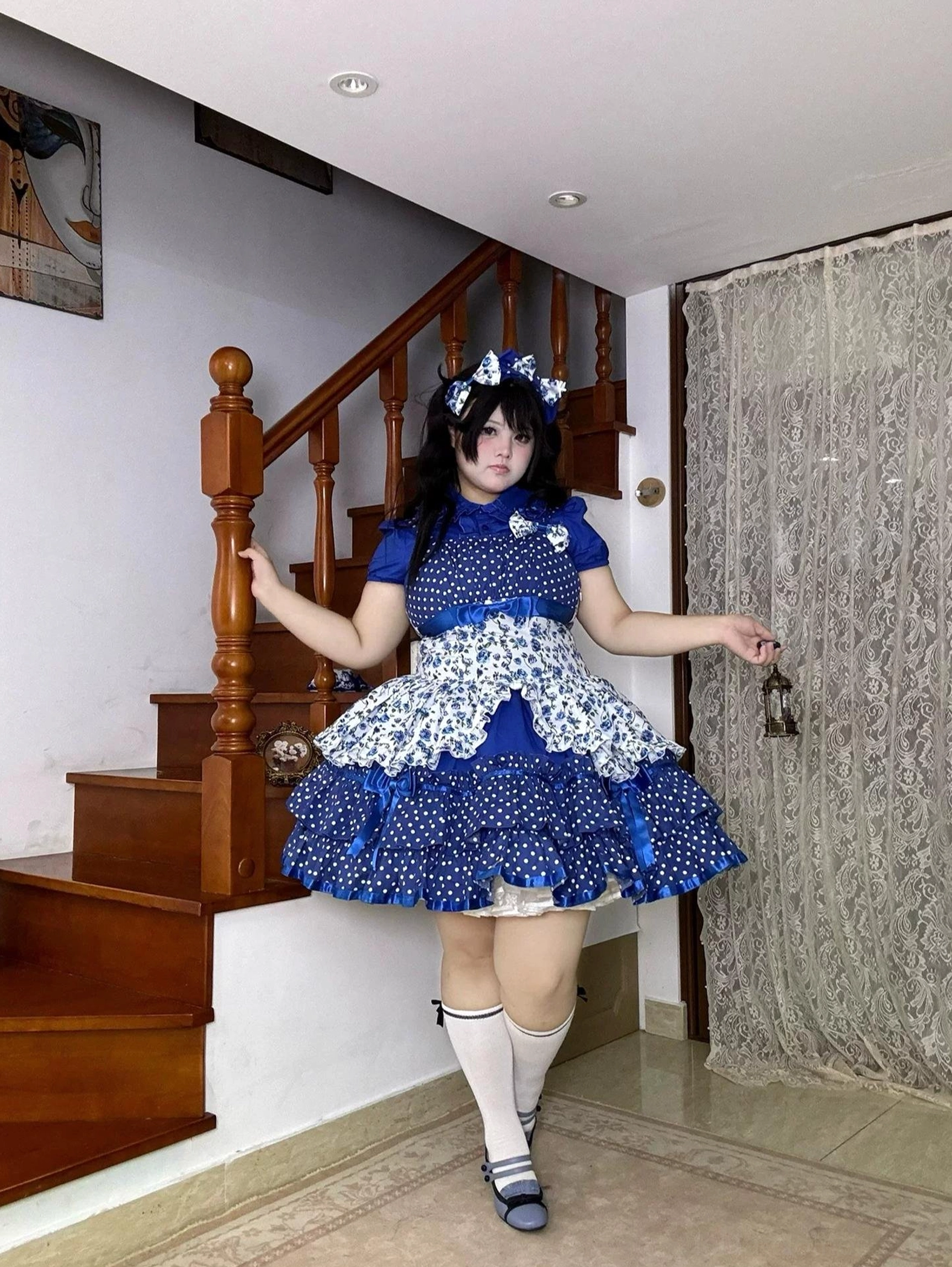 Blue polka dot and floral old school Lolita JSK dress full-body side view, dynamic pose on staircase with matching hair bow, knee-high white socks, Mary Jane heels, and holding decorative bell accessory