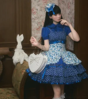 Blue polka dot and floral print old school Lolita jumper skirt with Peter Pan collar blouse, half-body side view featuring multi-tiered ruffled hem with satin ribbon trims and heart-shaped handbag accessory