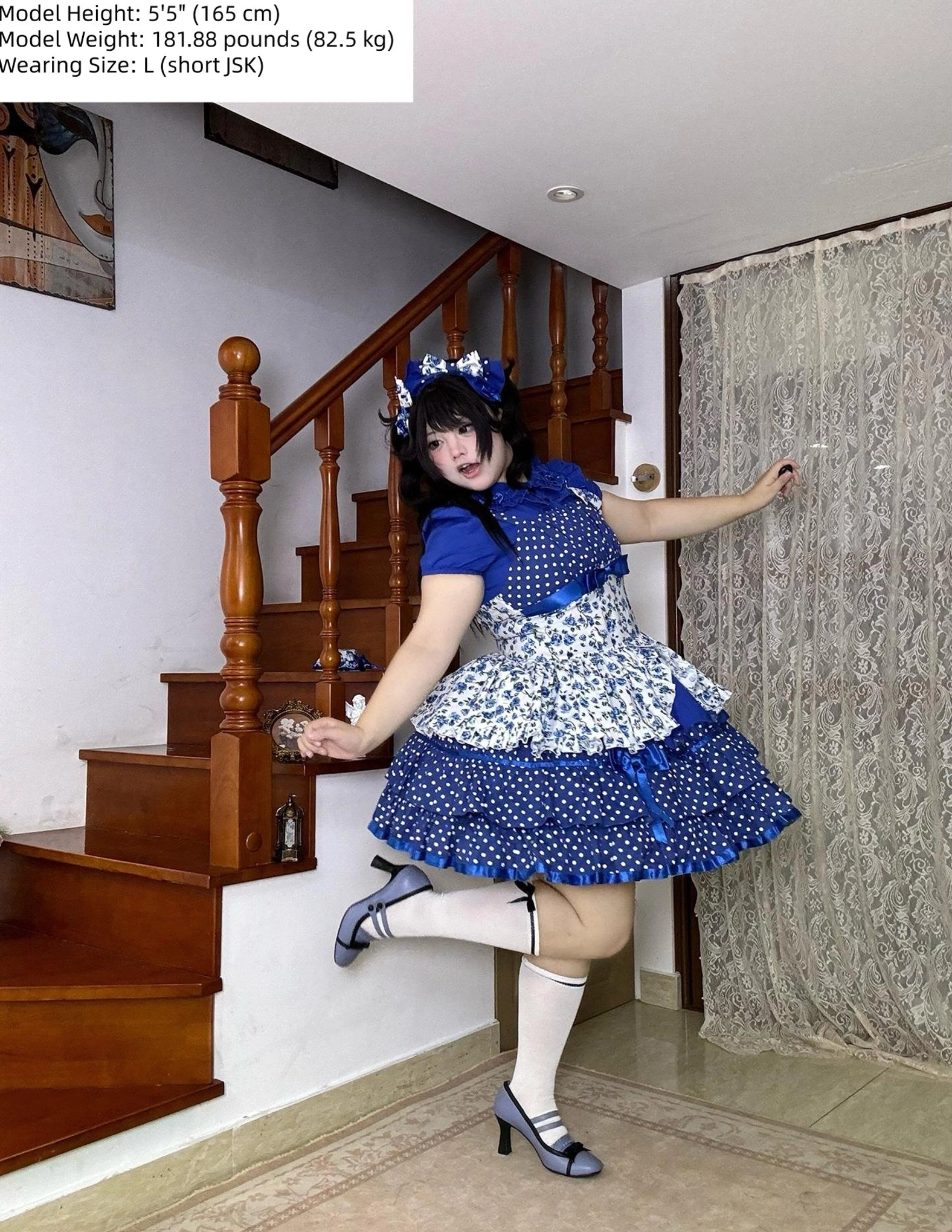 Blue polka dot and floral print old school Lolita JSK dress on model 165cm tall weighing 82.5kg wearing size L short JSK, full-body dynamic pose at home staircase with matching hair bow and Mary Jane heels
