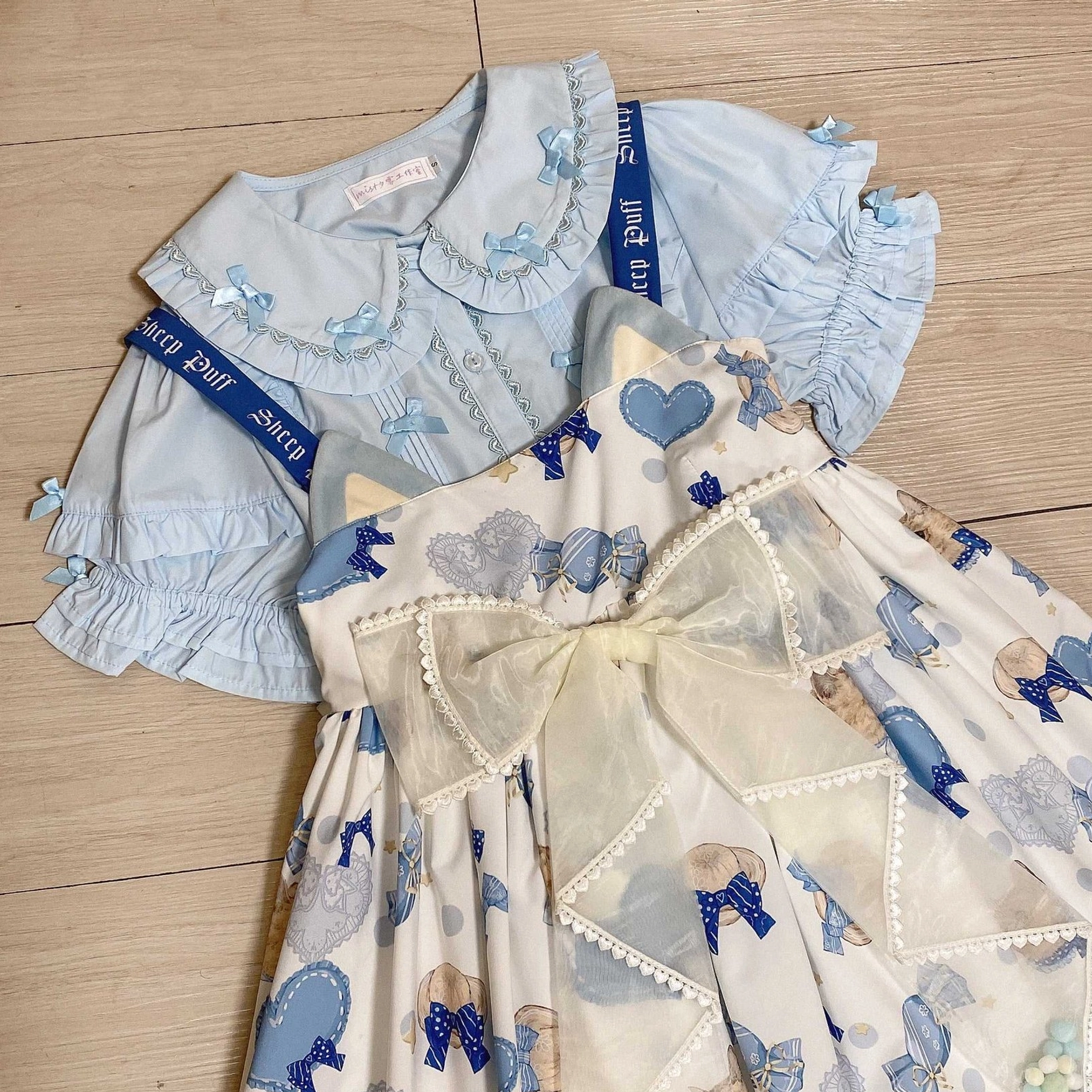 Blue two piece lolita outfit set with ruffled collar blouse bear heart print overall dress large sheer bow decor and branded sleeve ribbons flat lay