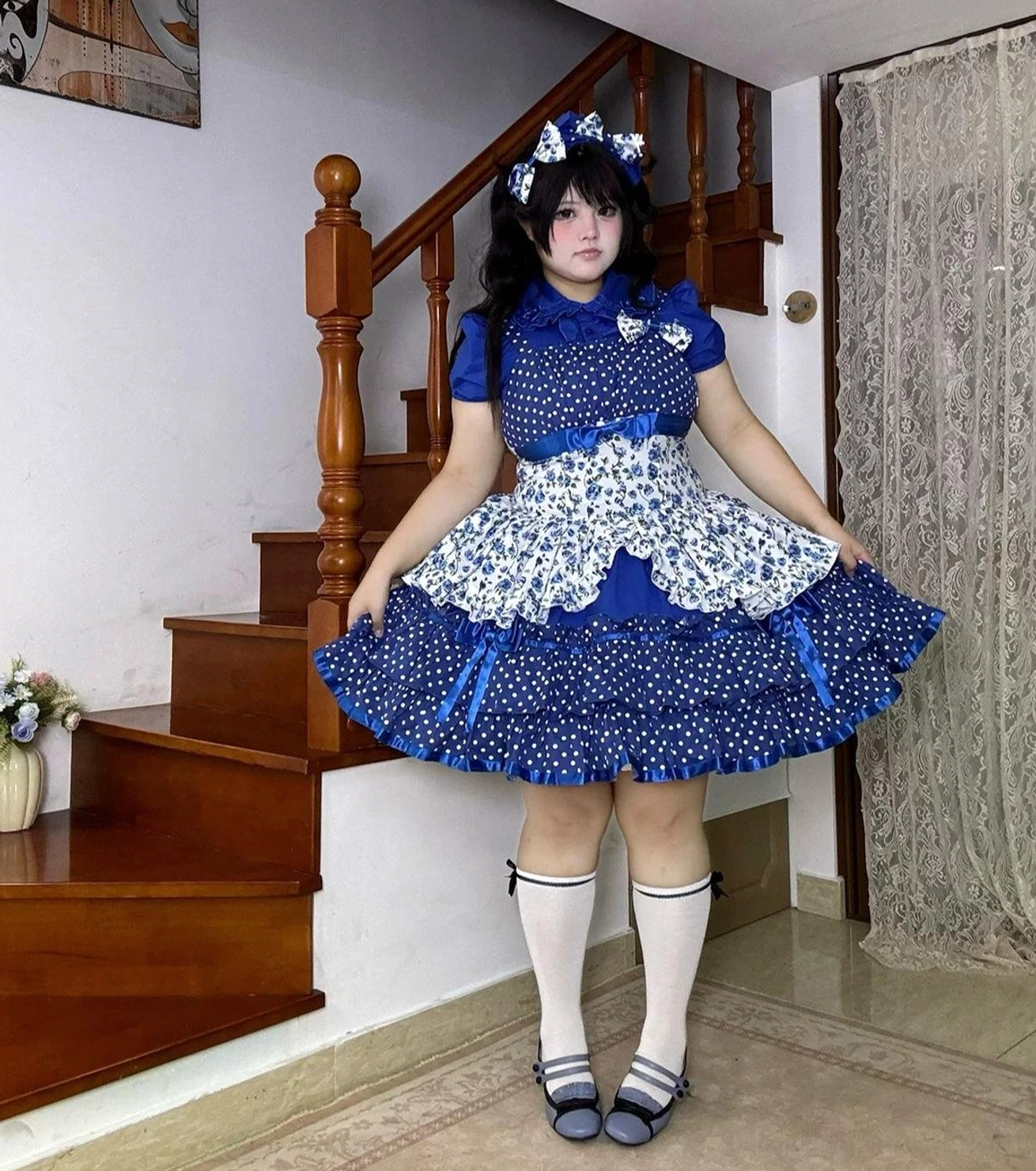 Blue old school Lolita jumper skirt with Peter Pan collar blouse, full-body front static view on staircase showing polka dot and floral print pattern, ruffled apron panel with satin trim details