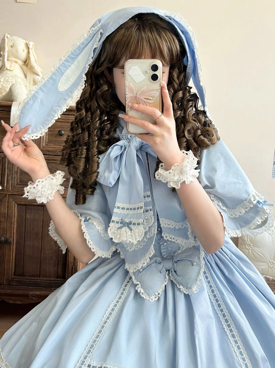 Sky blue rabbit ear hooded lolita cape dress mirror selfie front view curly brown model vintage wooden cabinet background lace trims white wrist cuffs