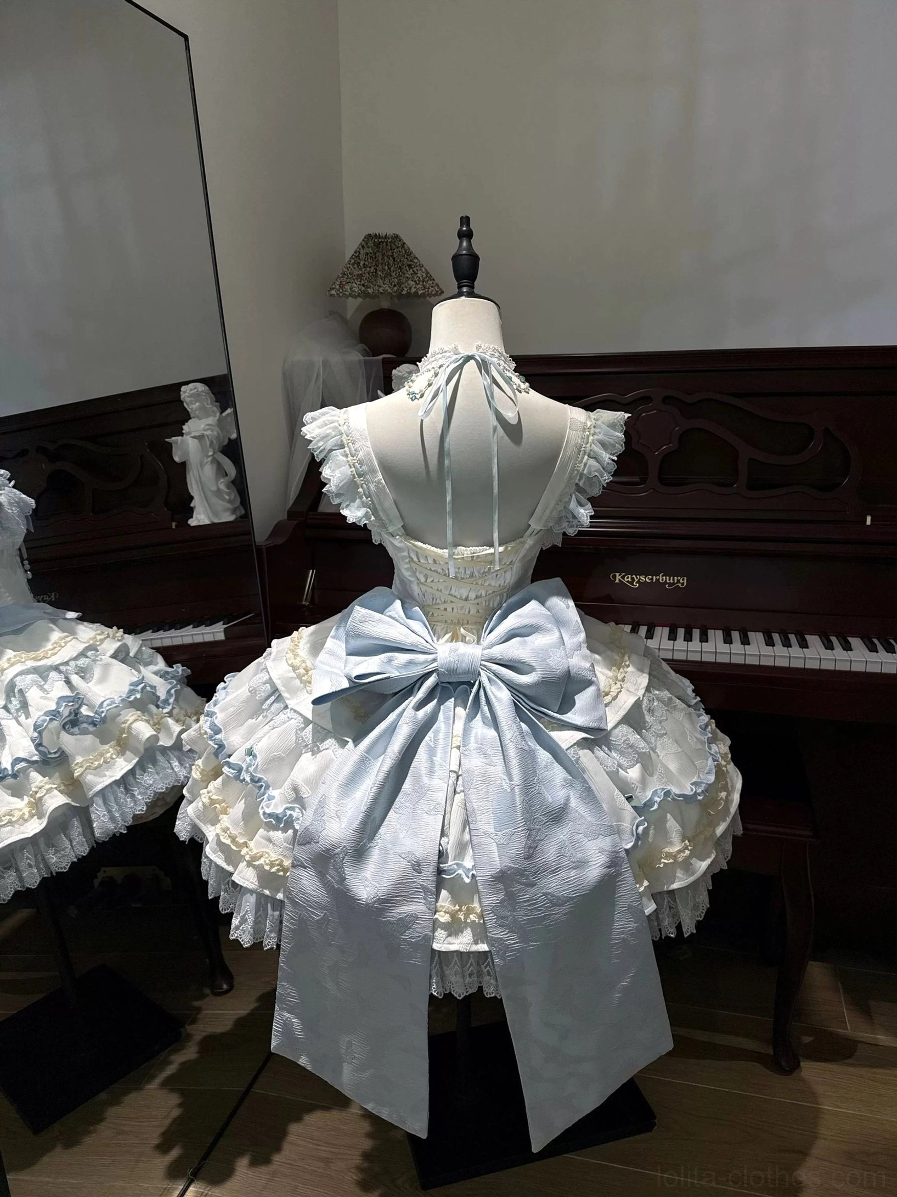 Back view of blue lolita JSK dress showing oversized detachable satin bow halter tie ruffled back straps matching tiered white lace skirt vintage piano studio
