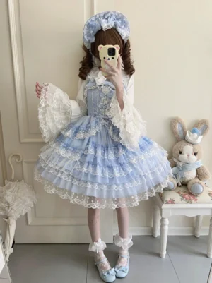 Blue Sweet Lolita jumper skirt with inner blouse mirror selfie front view featuring tiered lace skirt, matching blue bonnet, and flared lace cuffs in home interior space