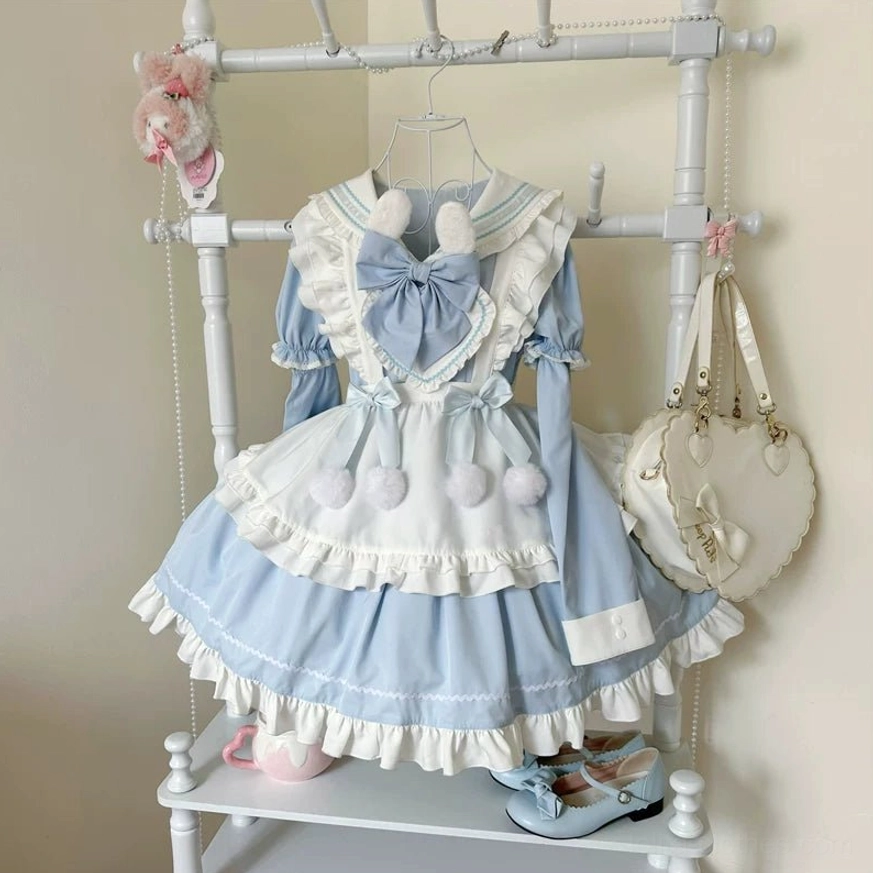 Blue and white maid-style lolita OP dress displayed on clothing rack with large chest bow, layered ruffled skirt, pom-pom waist decorations, and matching handbag, front flat display view