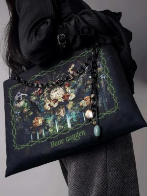 Bone Garden gothic lolita black canvas tote bag worn on model's arm, side oblique view showing full print and adjustable shoulder strap with dark gothic fashion coordination