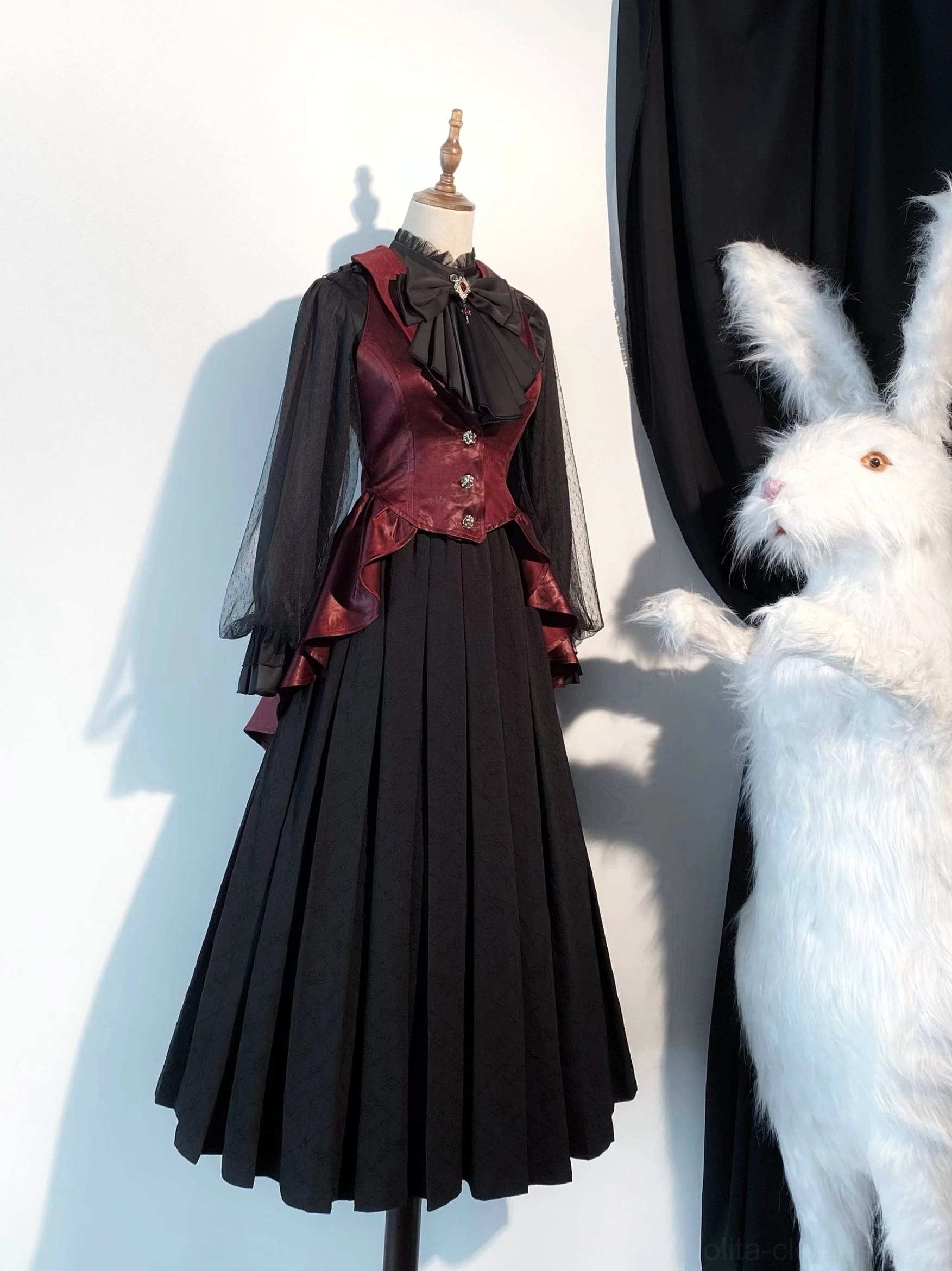 Black gothic lolita slim fit vest with bone-sword embroidery, sheer mesh sleeves, and long pleated skirt front three-quarter view on mannequin