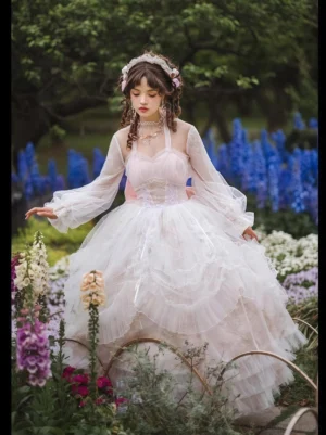 White bridal wedding lolita gown with halter open-back design and long sheer sleeves featuring floor-length tiered tulle ball skirt and floral hair ornaments in garden with delphiniums