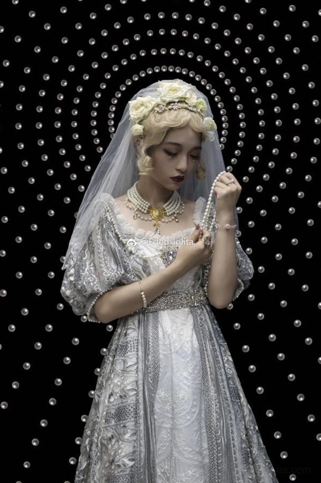 Elegant bridal woman in grey vintage gown with dark dotted circular pattern background, wearing pearl choker necklace with floral veil and curled hairstyle, delicately adjusting wrist jewelry in gentle regal pose