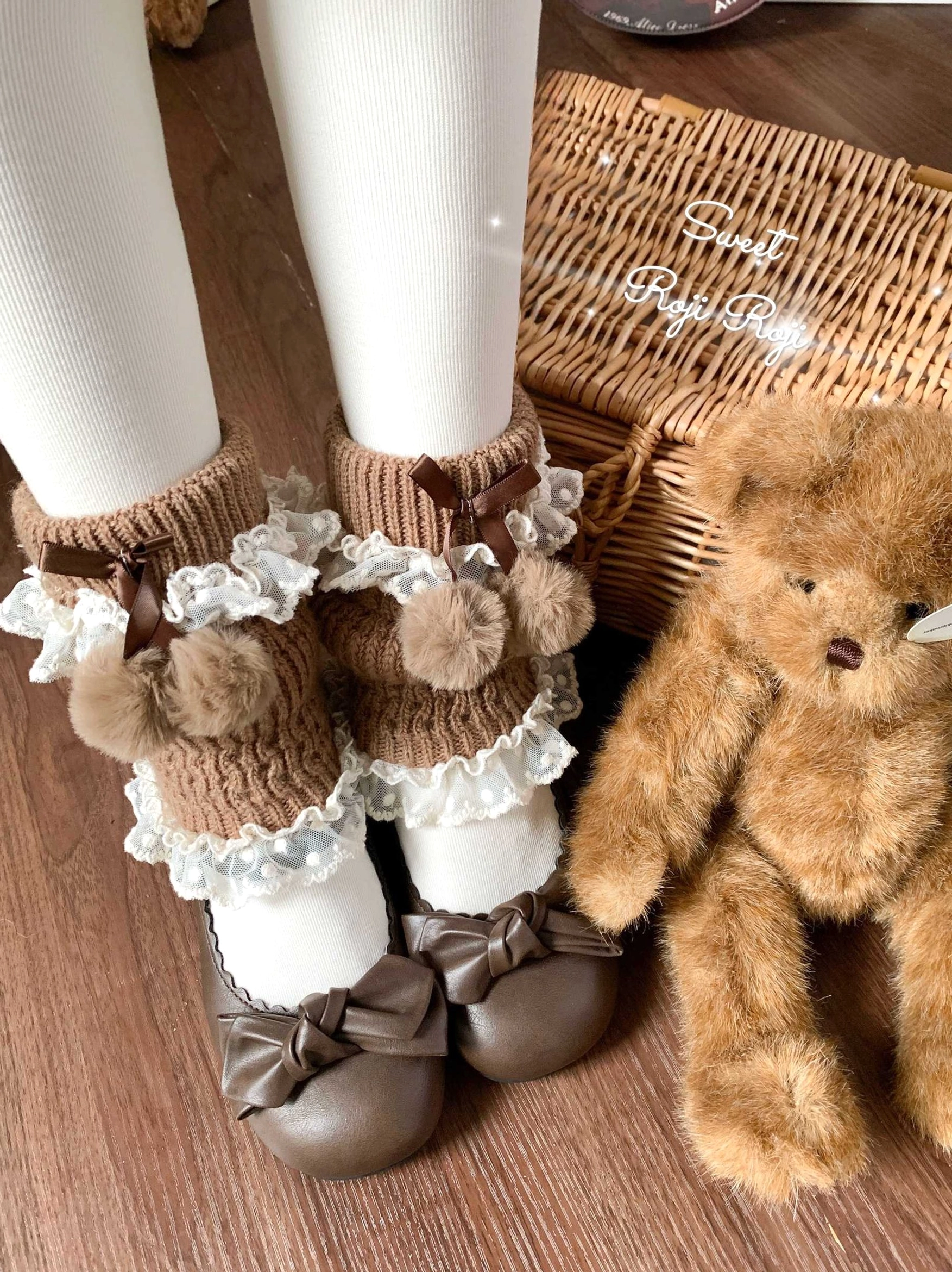 Brown lolita leg warmers with pom-pom accents and layered lace ruffles, three-quarter side view with wooden floor, wicker basket, teddy bear props