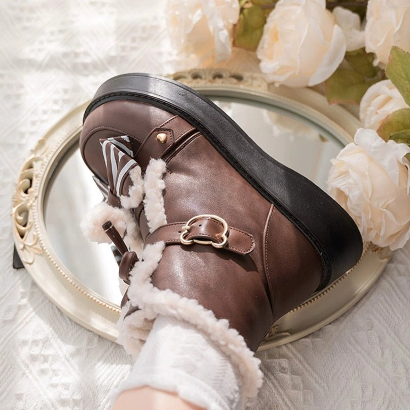 Side close-up view of brown lolita snow boot showing thick platform sole fleece lining leather strap with metal buckle and striped bow detail vintage mirror backdrop
