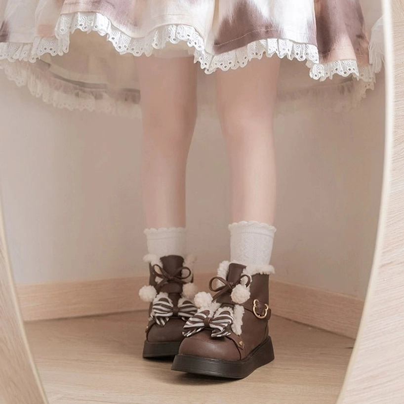 Low angle leg shot of dark brown lolita snow boots with fuzzy fur collar and striped bow decoration worn with white ruffled crew socks wooden floor background