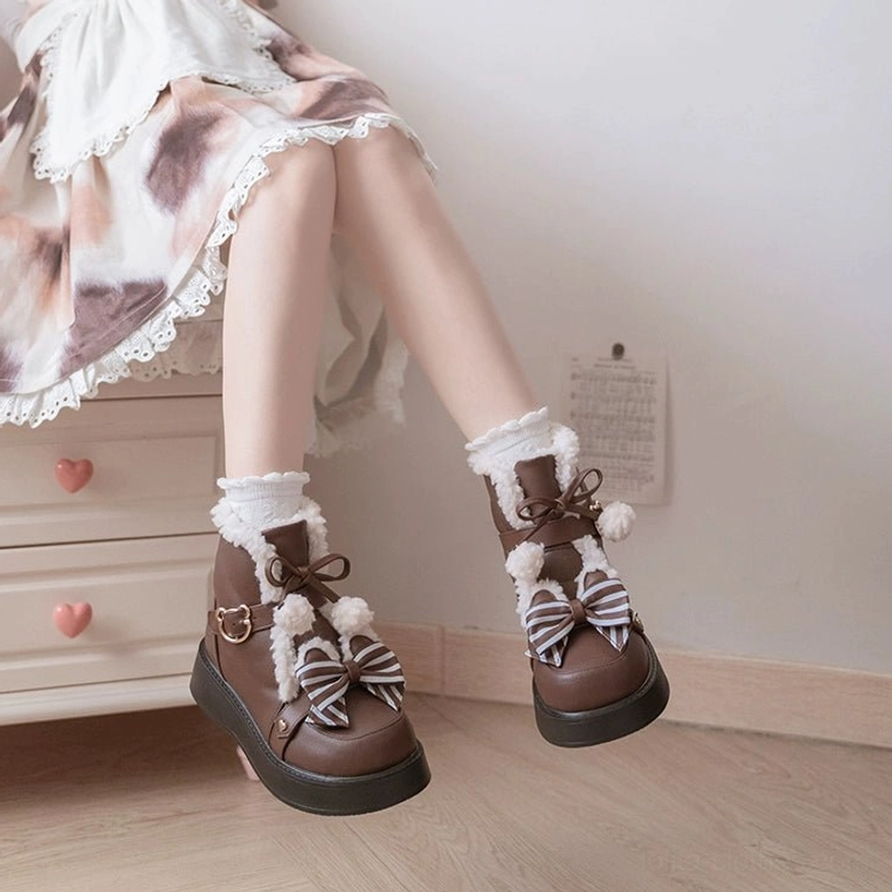 Side low angle shooting of brown lolita snow boots on model legs worn with tie-dye frilly lolita skirt warm fleece interior striped bow decorations