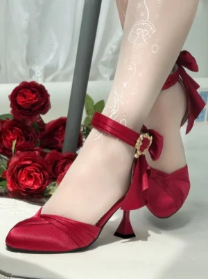 Burgundy classic Lolita wine glass heeled shoes with detachable bow and gold heart ankle buckle, worn with white patterned stockings and red rose decorative backdrop, side view of model's feet