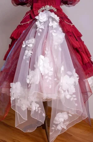 Lower skirt detail of burgundy classic lolita dress with asymmetrical sheer mesh train decorated with 3D white floral appliqués, pearl chain and rhinestone brooch embellishments