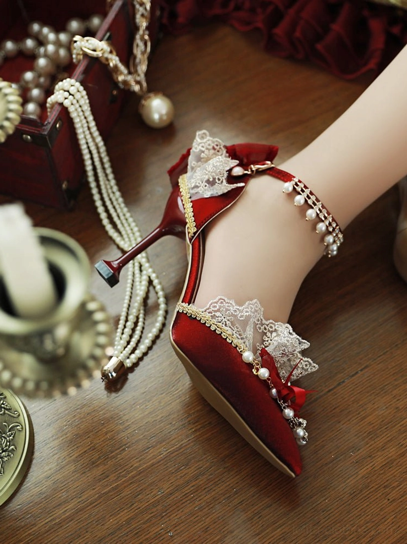 Model's foot wearing burgundy Lolita bridal heels side close-up, displaying pearl ankle strap chain, delicate lace heel trim, pearl and ribbon bow toe decoration, and refined stiletto heel