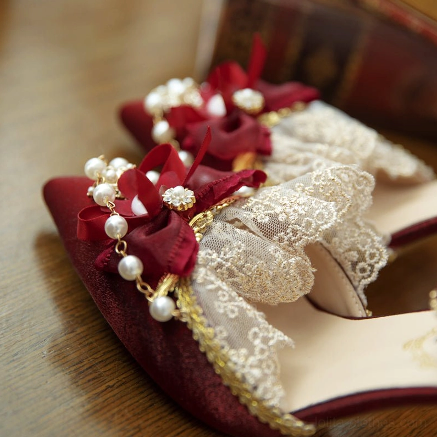 Close-up detailed view of burgundy Lolita wedding heels showing pointed toe, red pearl-decorated bow, lace trim accents, gold edge detailing, and velvet-like satin upper texture