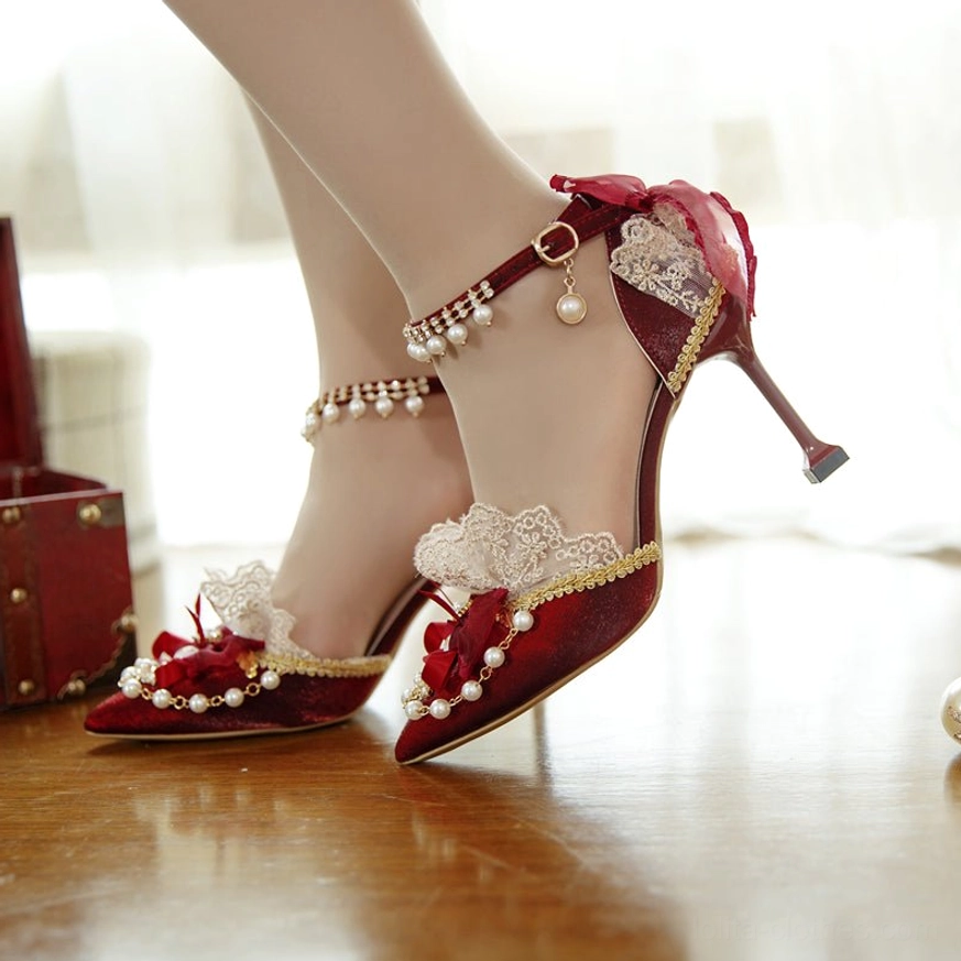 Model wearing burgundy stiletto Lolita bridal heels, close-up side view showcasing pearl ankle chain strap, lace heel collar, and thin pointed toe with red decorative bow