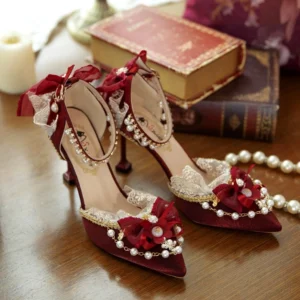 Burgundy pointed toe Lolita wedding heels with pearl bow decor, overhead flat lay on wooden table with vintage books and pearl accessories, showing intricate lace trim and gold edge details