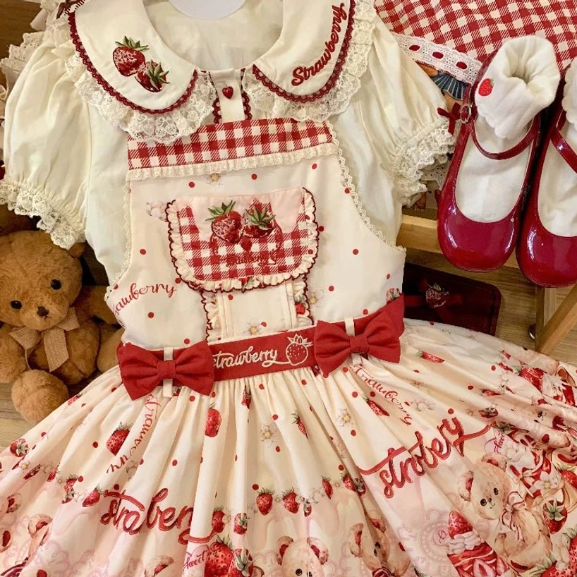 Burgundy-red sweet lolita salopette jumper skirt flat lay on blanket with red mary jane shoes and plush toys, gingham chest pocket, strawberry embroidery, bow waist sash