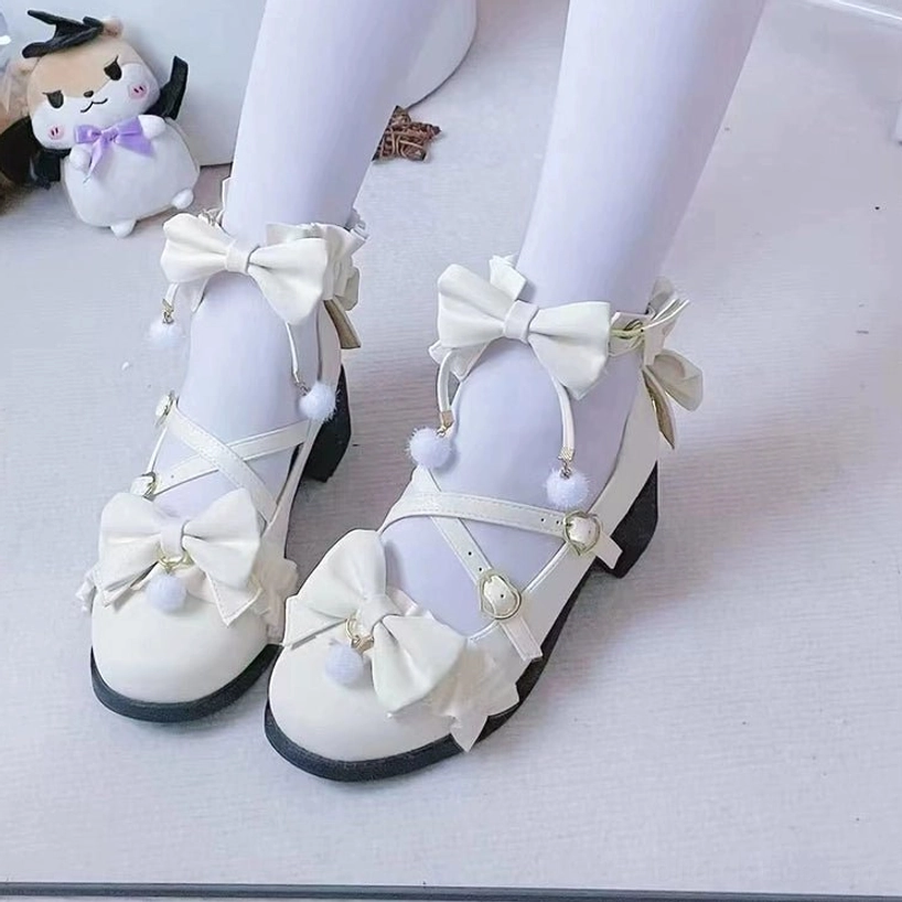 Off-white Lolita ankle strap butterfly bow shoes with pom-pom details and low block heel, worn with white sheer stockings, front overhead view on plain white floor