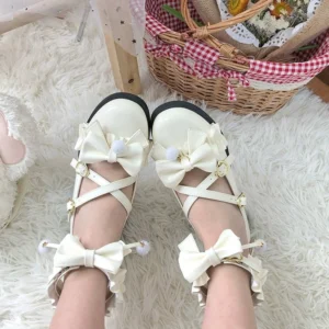 Off-white matte ivory Lolita Mary Jane shoes with butterfly pom-pom bows and cross ankle straps, overhead flat lay on cozy plush rug with vintage gingham picnic basket prop