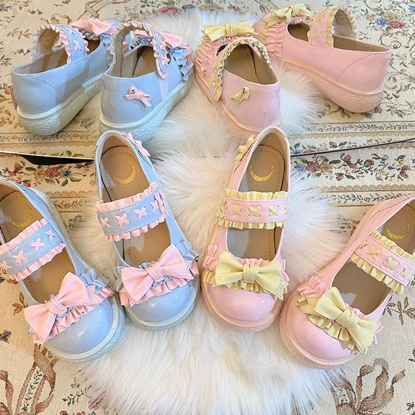 Overhead flat lay display of candy-colored Lolita shoes in baby blue and pastel pink with patent leather finish, satin bows and ruffled strap designs on vintage rug