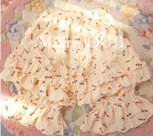 Candy print Lolita bloomers in beige with red decorative prints and double-layer ruffled hem design shown in flat lay front view on floral fabric backdrop