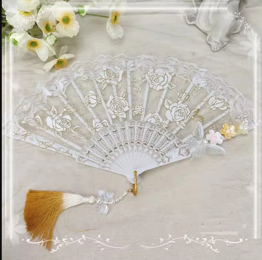 Carved frame lolita folding fan with rose embossed design featuring silver butterfly pink-yellow flowers and brown gradient tassel with pearl detail on fabric backdrop
