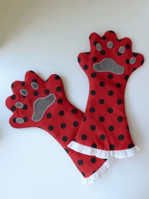 Cat paw gloves with red polka dot fabric, grey embroidered paw pads, and white ruffled cuffs, flat lay top-down view on white background