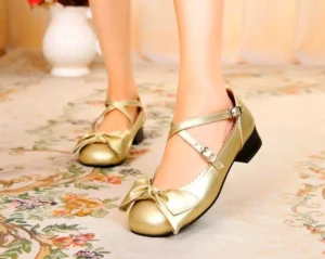 Champagne gold bow cross-strap lolita leather shoes front three-quarter view on model wearing vintage floral carpet background