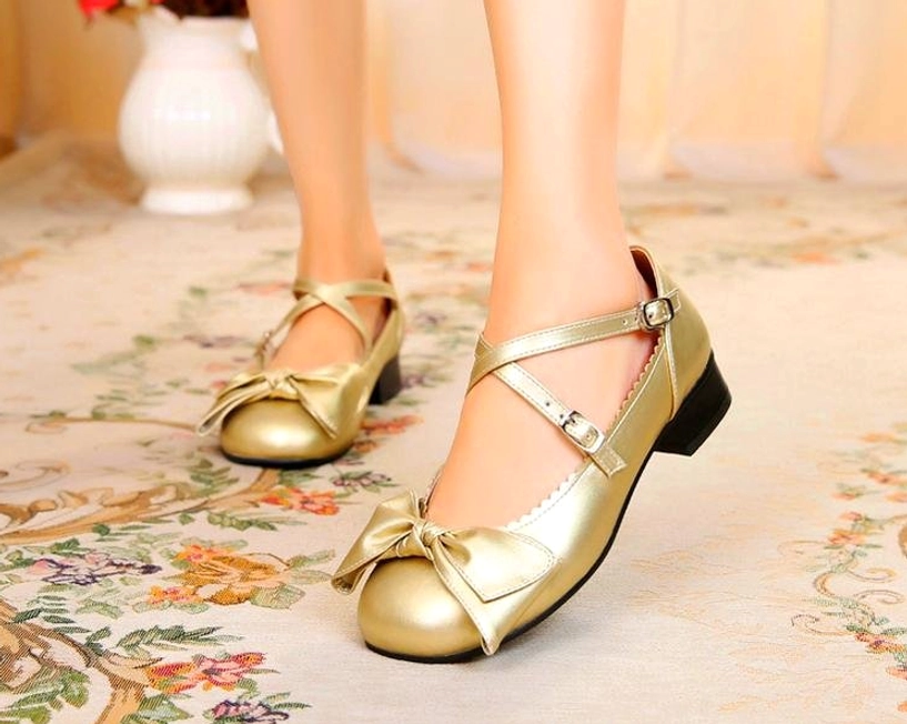 Champagne gold bow cross-strap lolita leather shoes front three-quarter view on model wearing vintage floral carpet background