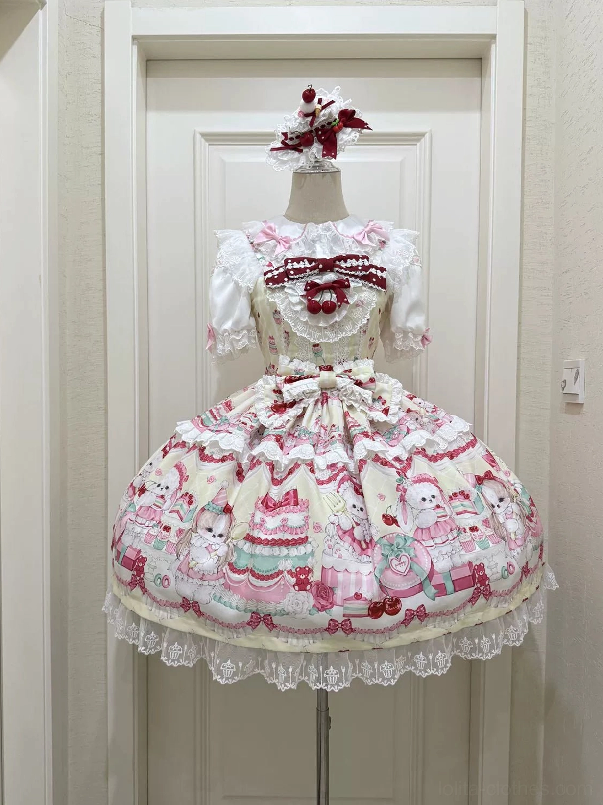 Cherry Bake Song Lolita JSK Dress in deep pink colorway on dress form, flat display front showing heart-shaped bow on lace collar, large waist bow accent, all-over dessert and animal print composition