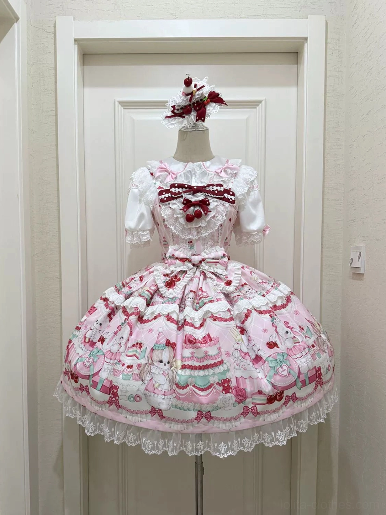 Cherry Bake Song Lolita Jumper Skirt in light pink white on dress form, flat front display showing white lace collar with red bow, delicate animal and cupcake prints throughout skirt, embellished lace trim