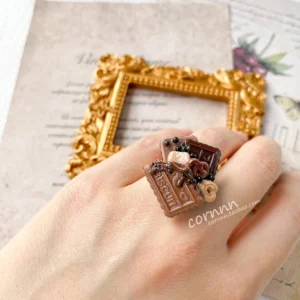 Side view of chocolate cookie themed adjustable Lolita ring on hand showing layered biscuit charms, glossy chocolate sauce, and open adjustable ring band