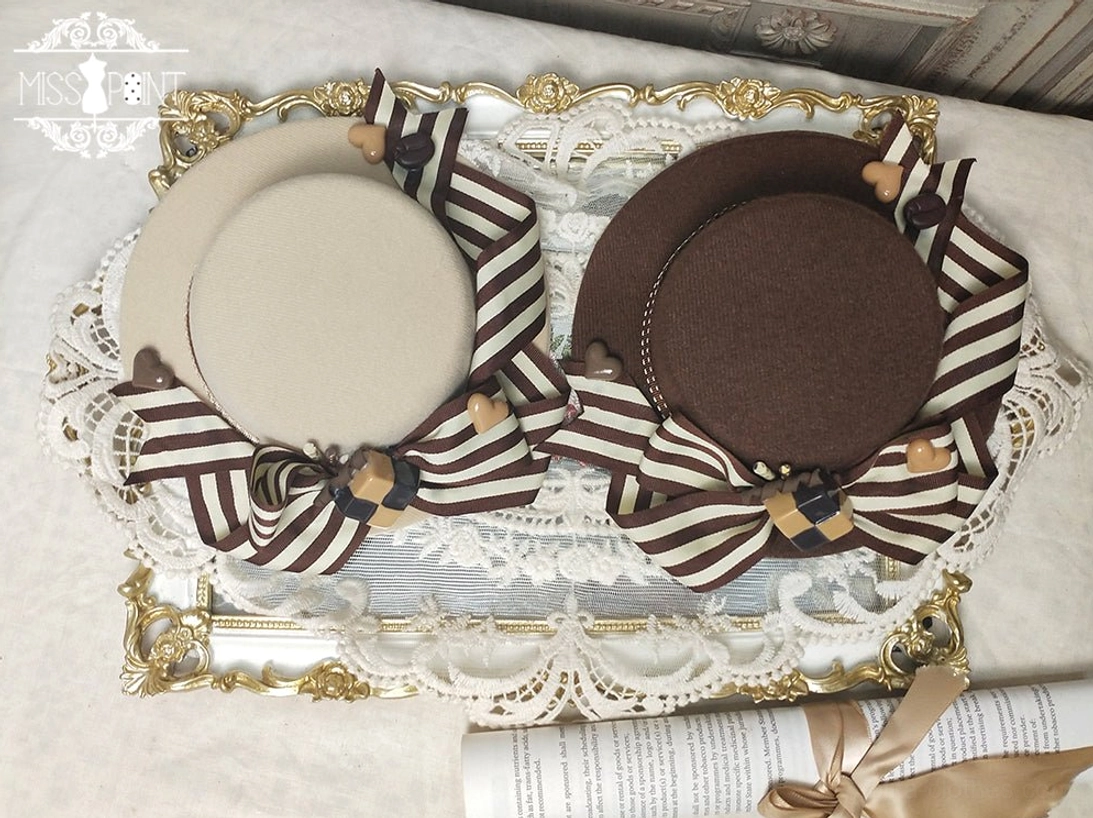 Single style sweet lolita flat-top hat with striped bow, decorative charms, and biscuit ornaments showcased in top-down close-up flat lay view on gilded tray with lace mat background, two color variations
