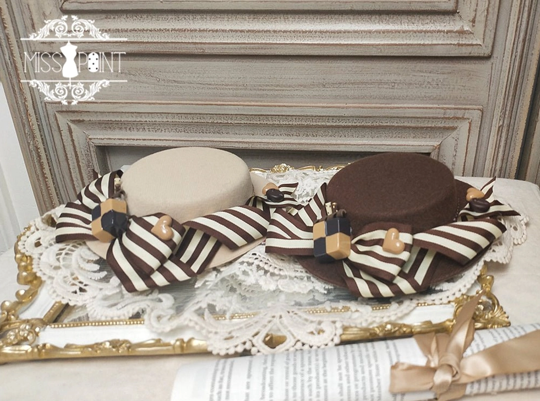 Top-down flat lay product display of two-piece chocolate daily sweet lolita hat collection featuring beige and dark brown flat-top hats, both with striped bows and biscuit-themed decorations on retro photo frame and lace placemat