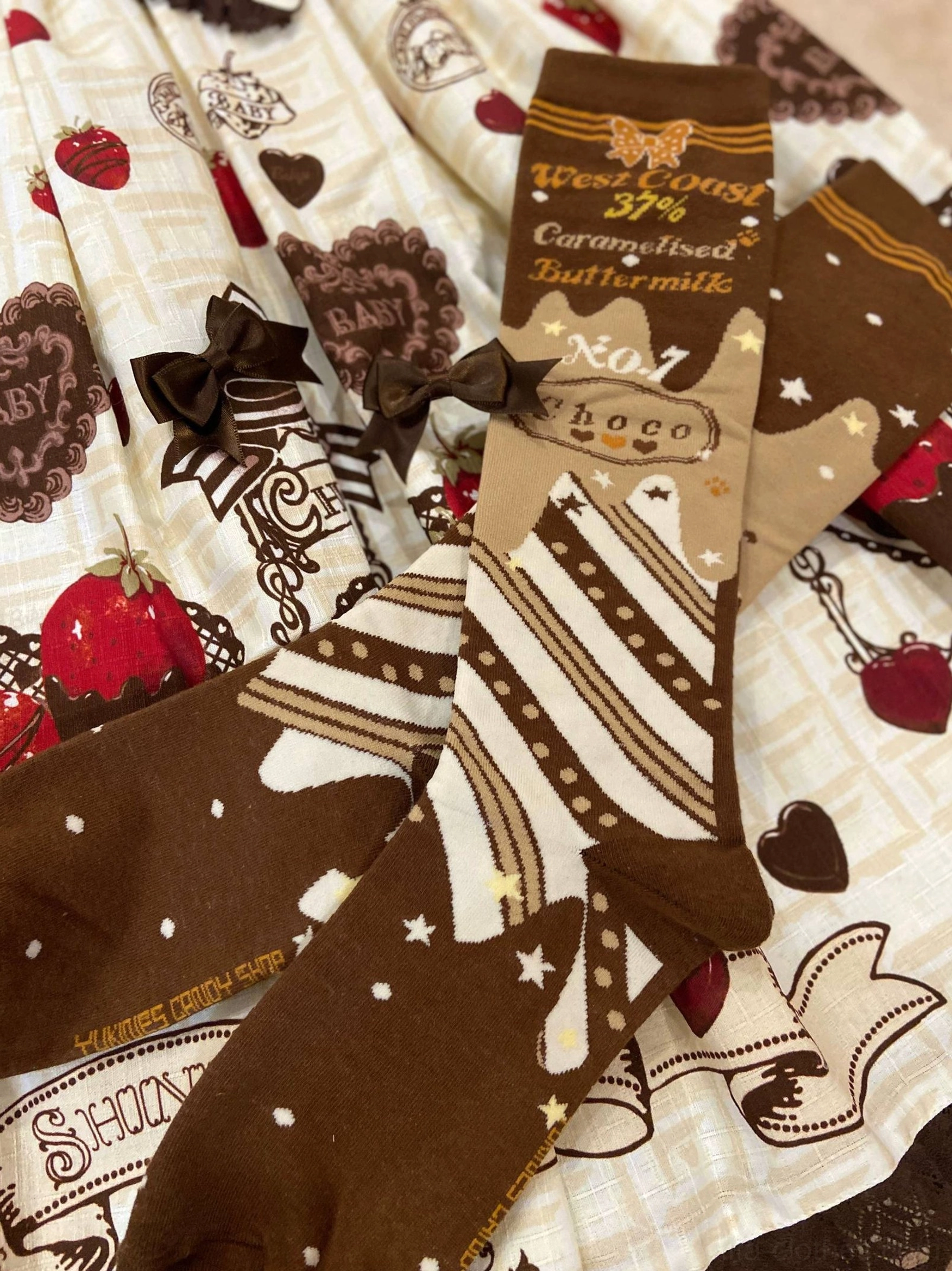 Over-the-knee chocolate lolita socks overhead flat lay with sweet strawberry print fabric background and star dot patterns