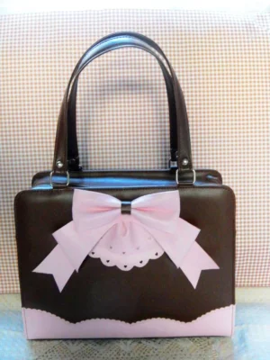 Chocolate pink two-tone Lolita PU top handle handbag with large bow and lace cutout detail on gingham backdrop