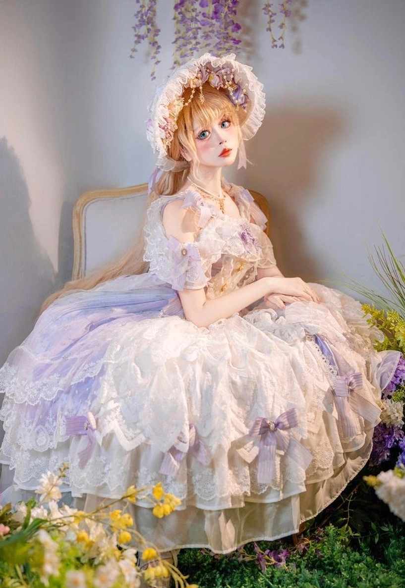 Classic bridal lolita JSK dress three-quarter side sitting pose among floral greenery, showcasing lavender tulle underlayer with off-white lace overlay, purple ribbon bows on skirt hem, and matching floral headpiece accessory